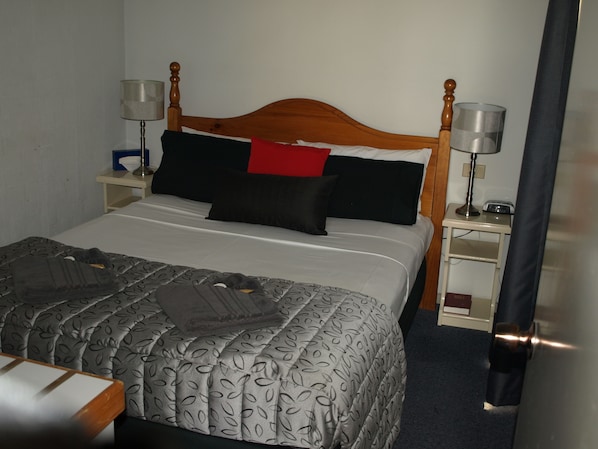 A neatly made bed with a patterned bedspread, two bedside lamps, and a nightstand with a radio. - Old Coach Motor Inn Echuca (Echuca)