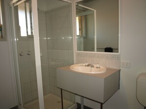A bathroom with a glass-enclosed shower, a sink with a mirror above it, and a tiled floor. - Old Coach Motor Inn Echuca (Echuca)