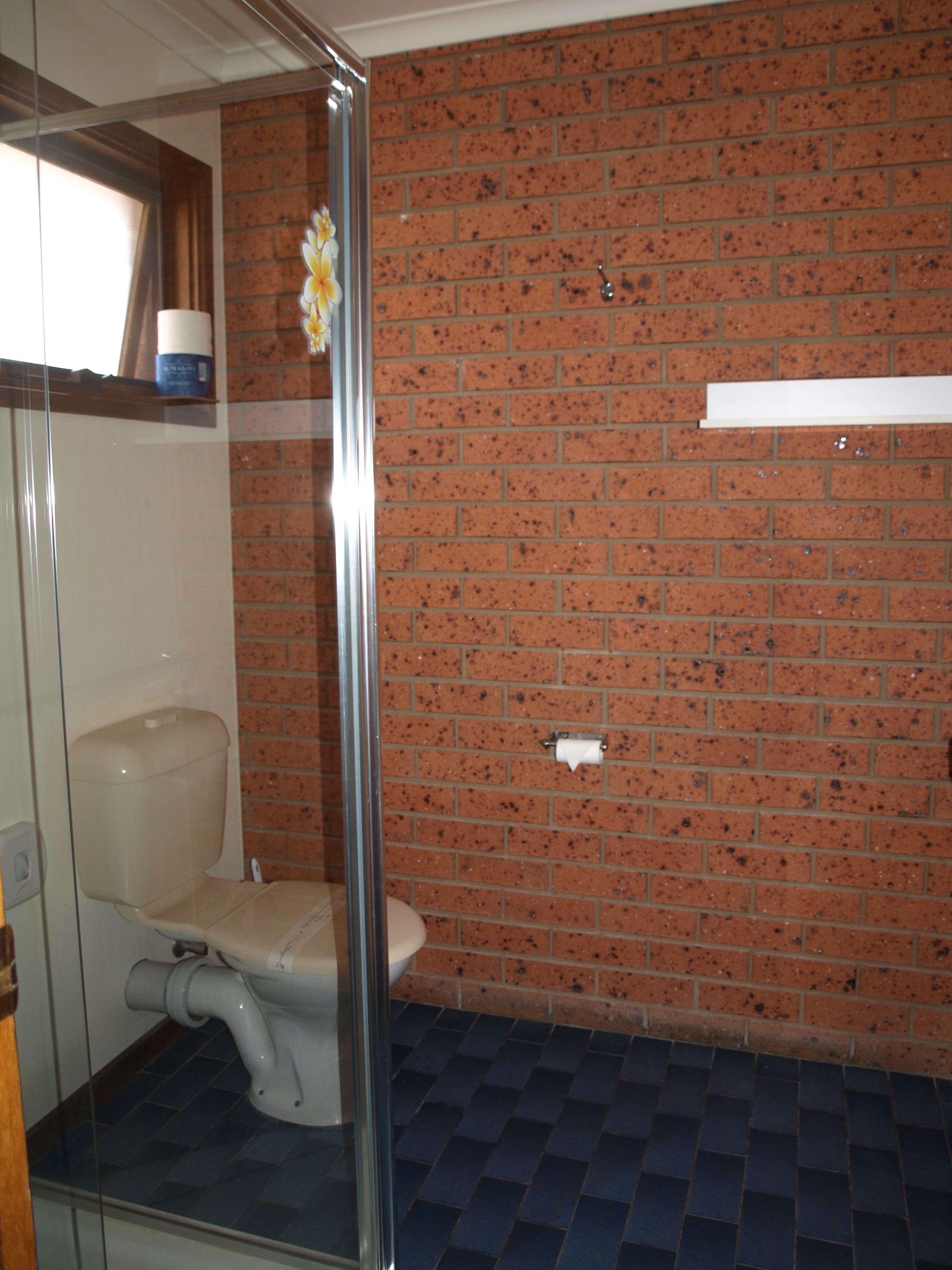 Een badkamer met een douchecabine van glas, een toilet en een bakstenen muur.