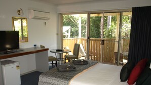 Habitación de hotel con cama, escritorio con televisor, refrigerador pequeño y balcón con sillas y mesa.
