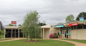 Un bâtiment sur lequel on peut lire l’enseigne « Carlton Draught Rubicon Bistro », ainsi qu’une poste et un petit espace jardin agrémenté d’un arbre et de fleurs.