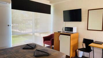 A hotel room with a bed, a desk with a computer, a microwave, a TV, and a small refrigerator.