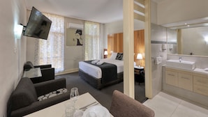 A hotel room with a bed, a desk with a chair, a sofa, a TV, a bathroom with a sink and mirror, and a shower. - Rose City Motor Inn (Benalla)