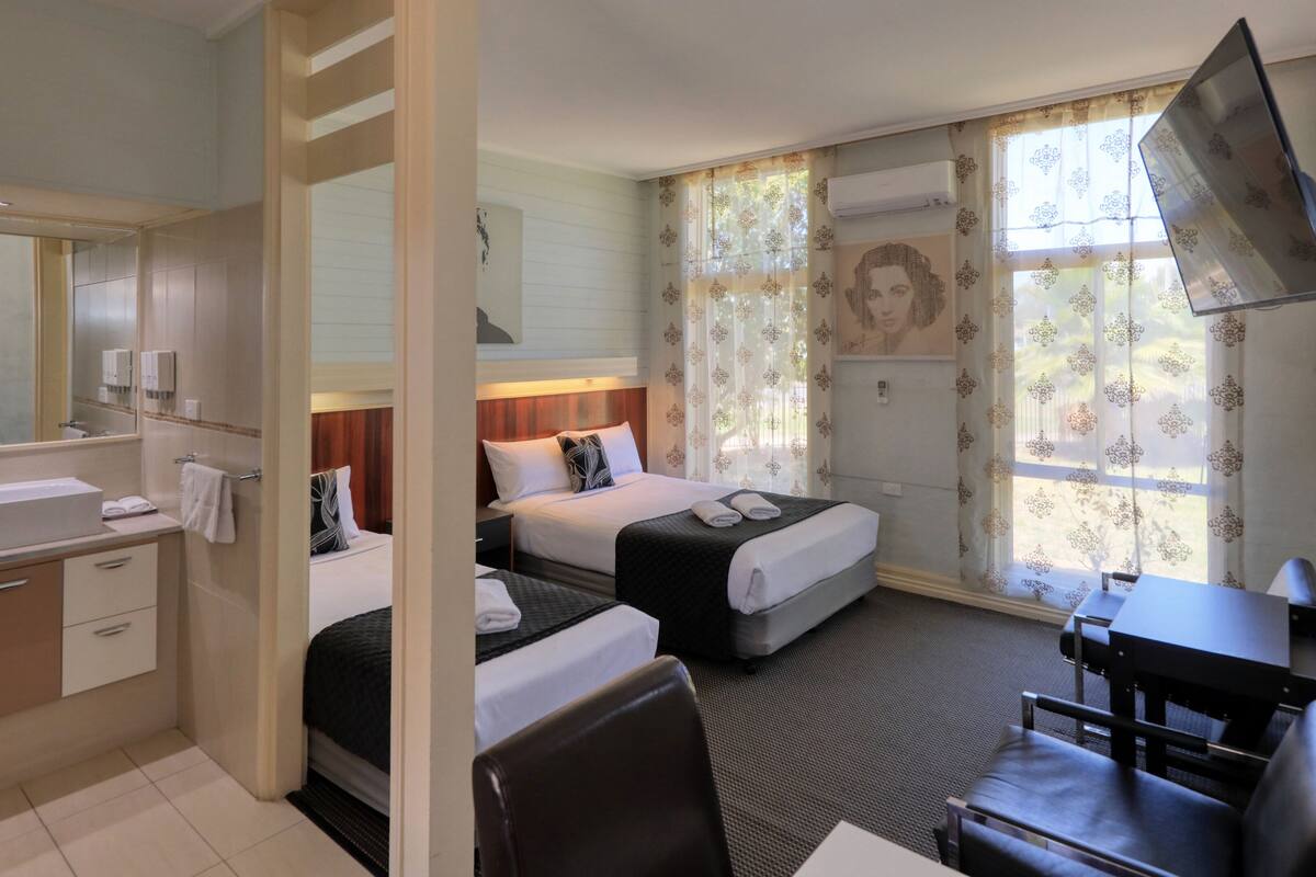 A hotel room with a bathroom, two beds, a desk, and a TV.