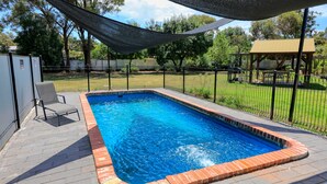 A rectangular swimming pool with a brick edge, surrounded by a paved deck and a black metal fence. - Rose City Motor Inn (Benalla)