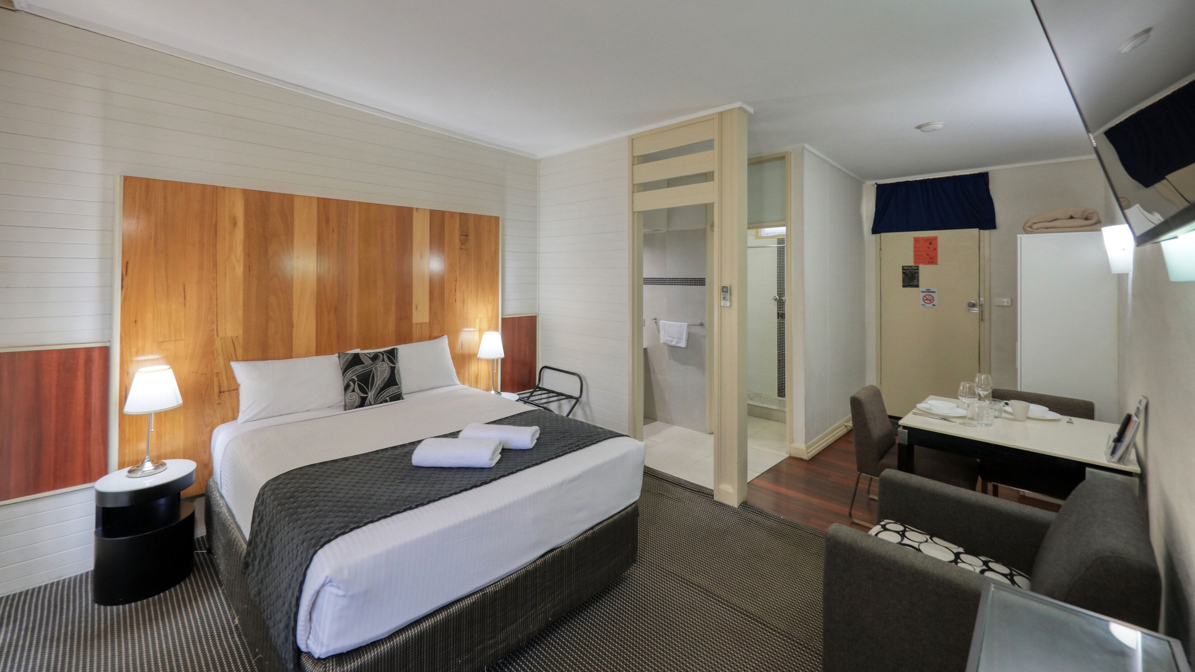 A hotel room with a bed, bedside tables, a desk, a chair, and a mirror.