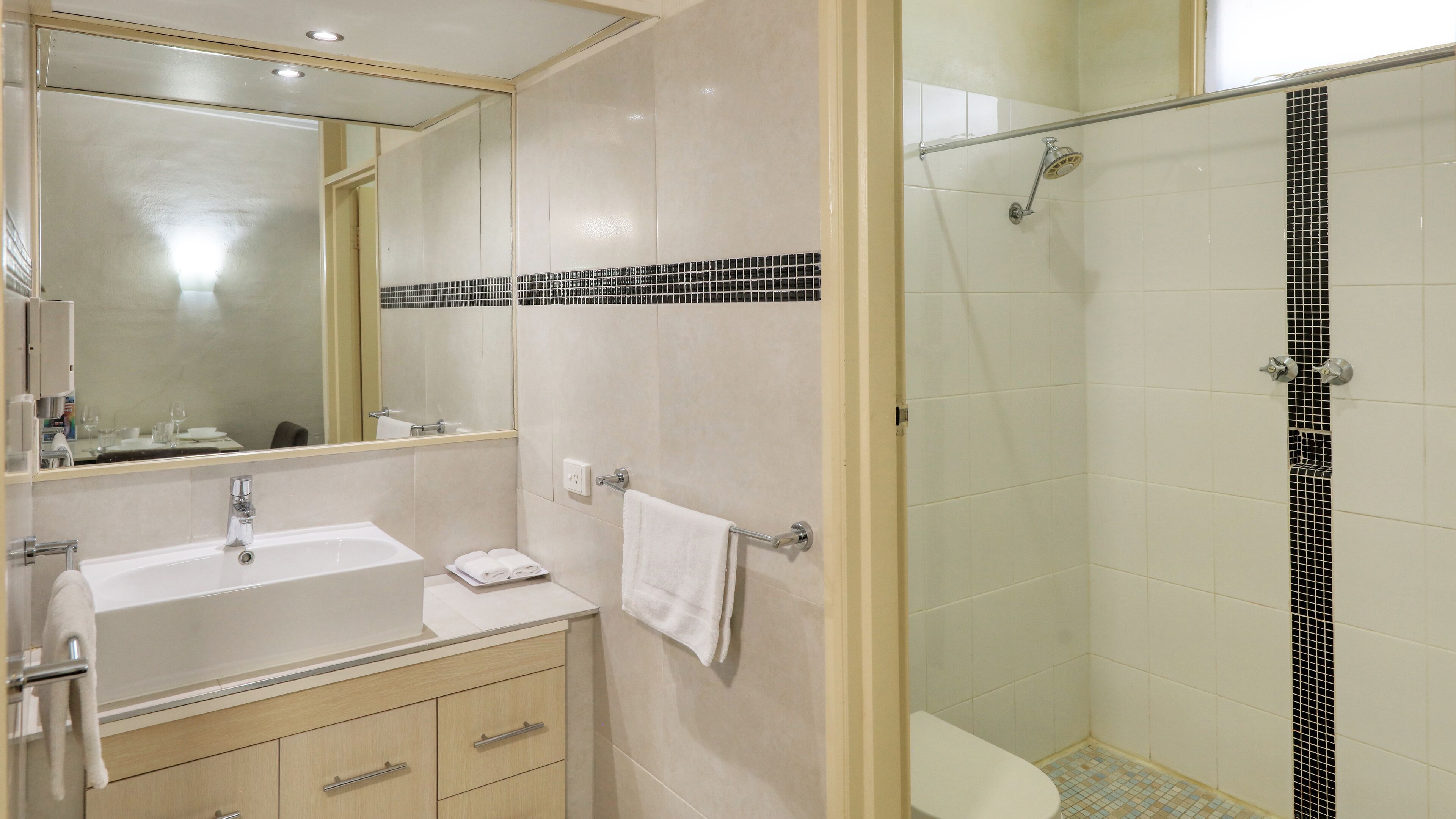 A bathroom with a sink, mirror, towel rack, and shower area.