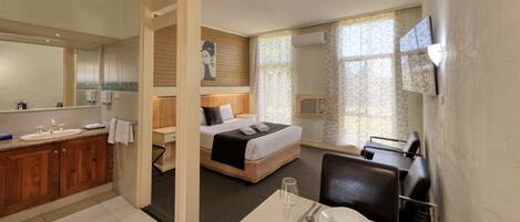 Hotellihuone, jossa on puinen peilipöytä, sängynpäätyyn varustettu sänky, työpöytä tuolilla ja ruokapöytä, joka on katettu kahdelle.