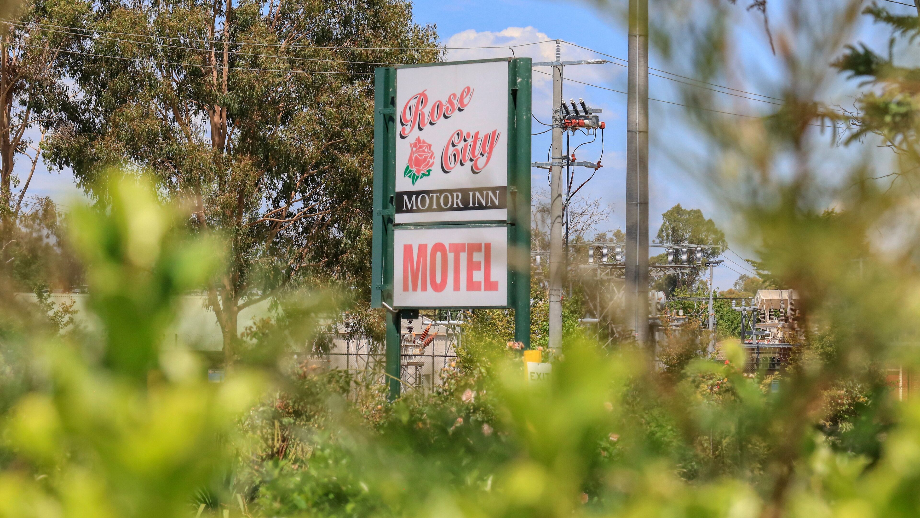 A motel sign with "Rose City Motor Inn" and "Motel" written on it, surrounded by greenery.