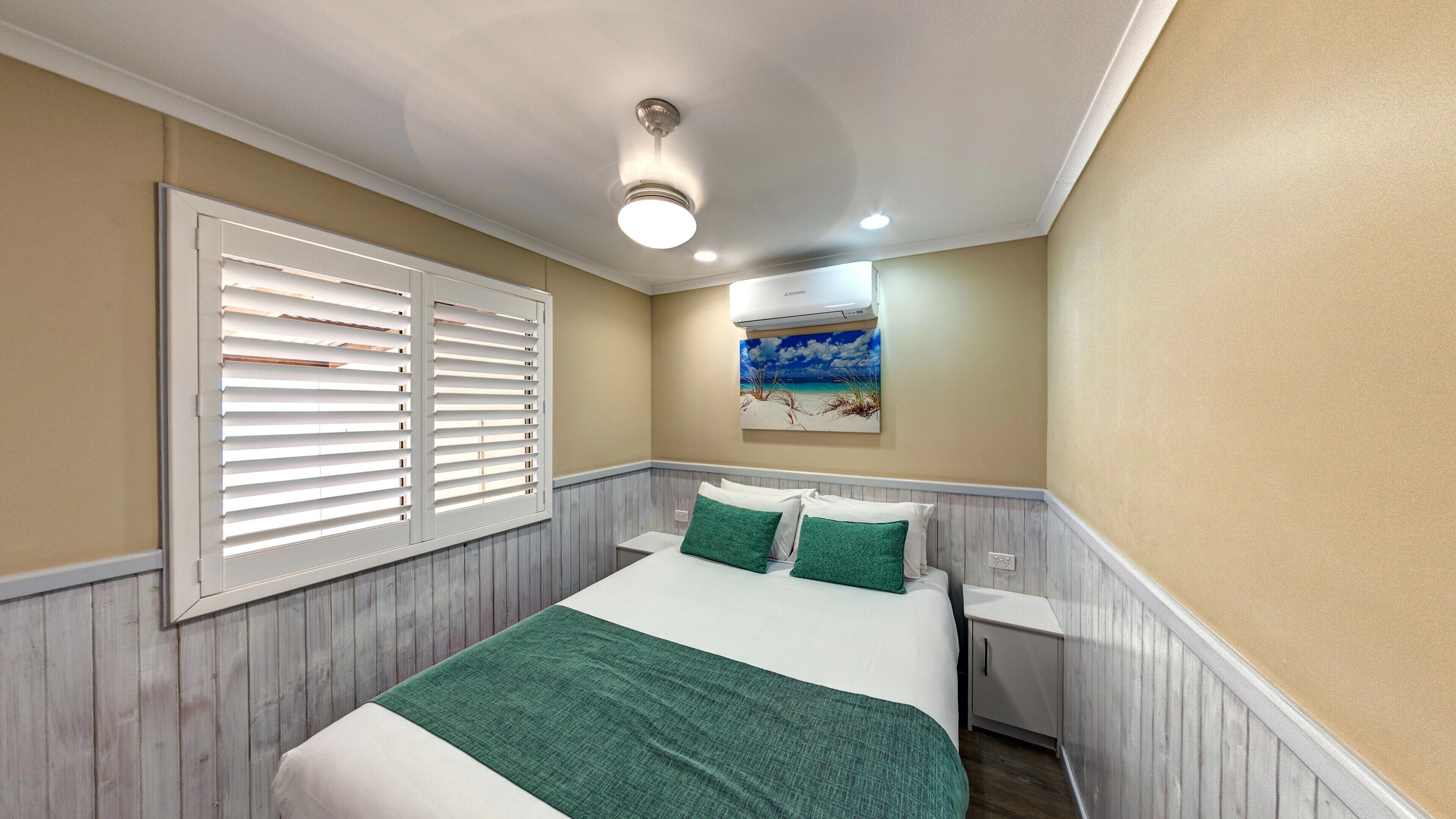 Un dormitorio con cama, mesita de noche, aire acondicionado de pared y un cuadro con motivos marinos.