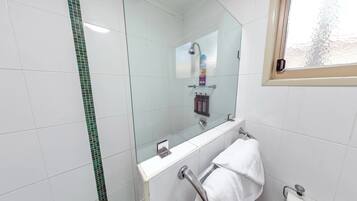 A modern bathroom with white tiles, a glass shower enclosure, a white towel rack, and a window with a view of trees.