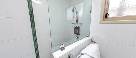 A modern bathroom with white tiles, a glass shower enclosure, a white towel rack, and a window with a view of trees.