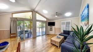 Un salón amplio con suelo de madera, un sofá azul, una mesita de centro y un televisor fijado a la pared.