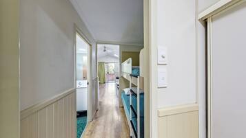 A narrow hallway with bunk beds on the right, a door on the left, and a bathroom visible in the distance.