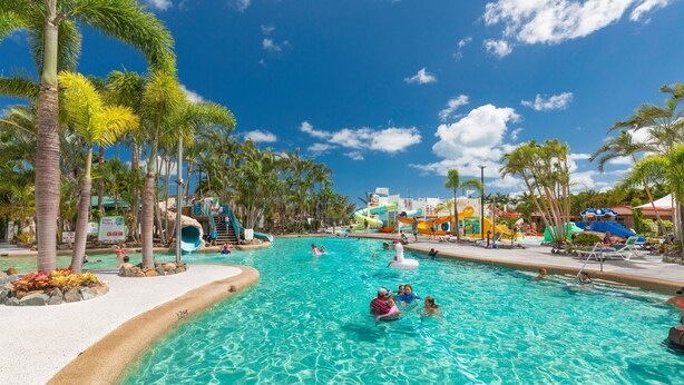 Una gran piscina al aire libre rodeada de palmeras y un tobogán.