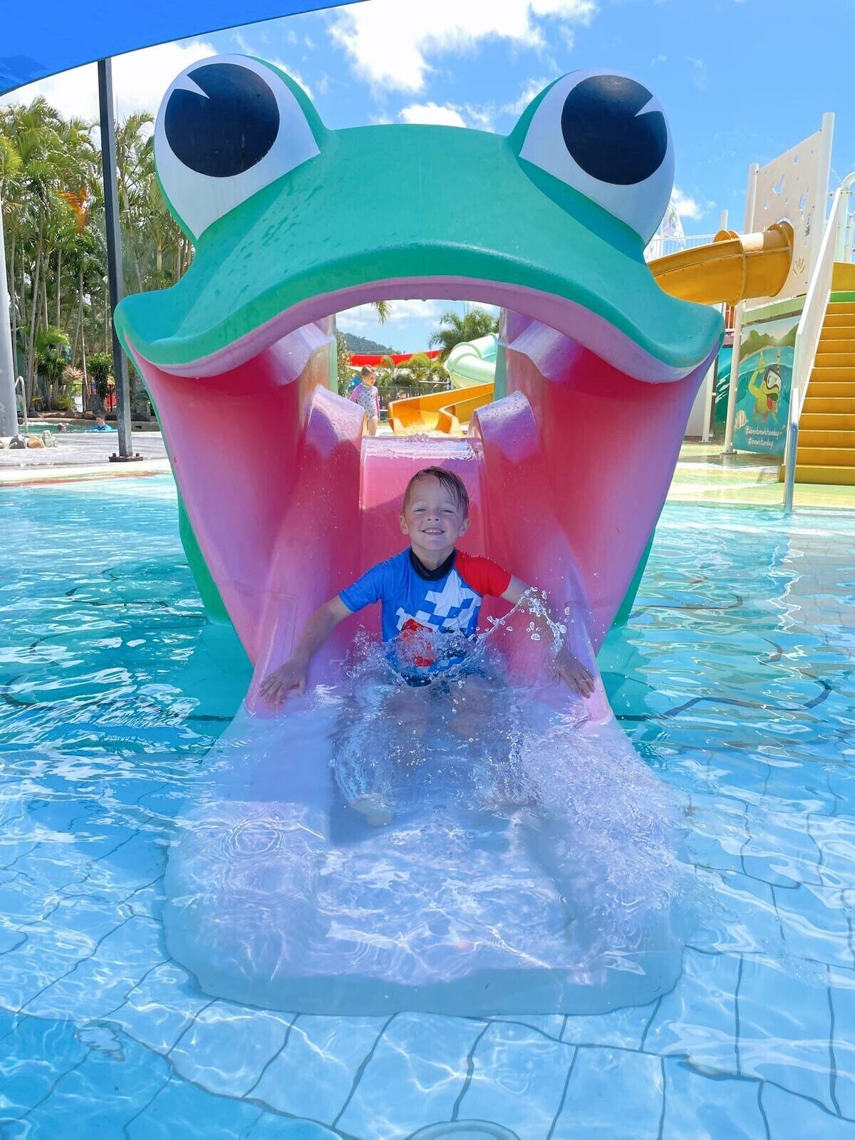 A child sliding down a water slide shaped like a frog's mouth.