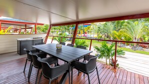 Un patio al aire libre con mesa y sillas, una parrilla y vistas a un jardín tropical.