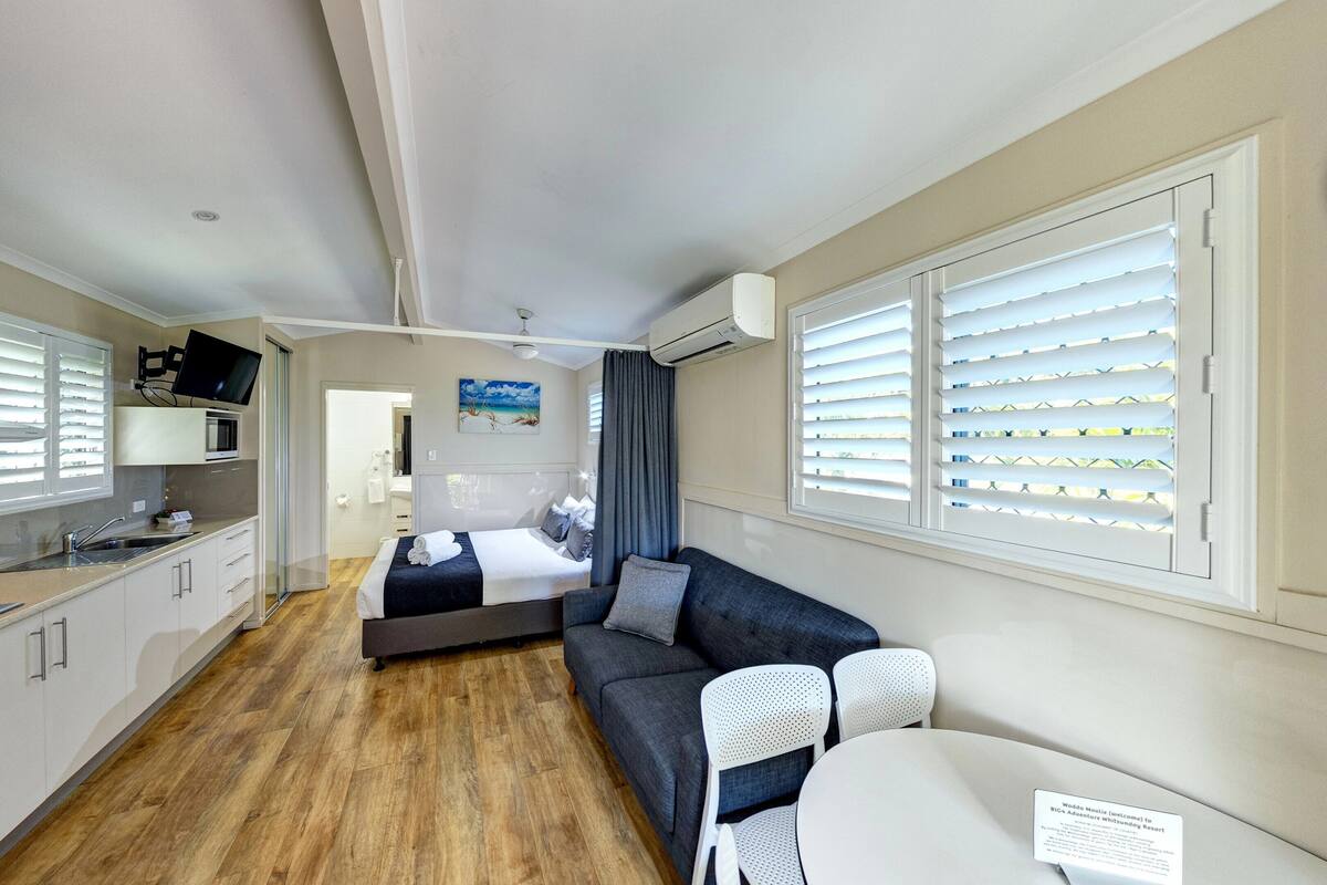 Habitación de hotel compacta con kitchenette, cama, sofá y zona de comedor.