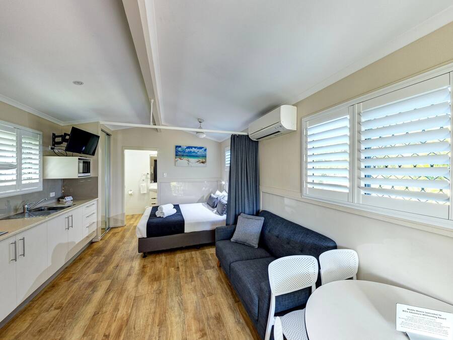 A compact hotel room with a kitchenette, a bed, a sofa, and a dining area.