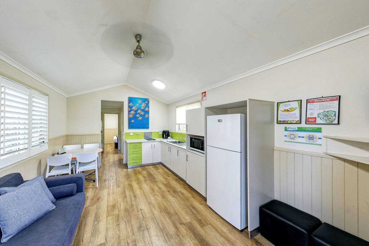Cocina compacta con refrigerador, pileta y microondas. Hay un comedor con mesa y sillas, y un sofá con almohadones.