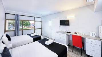 A hotel room with two beds, a desk, a chair, a TV, and a window with curtains.