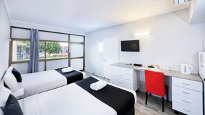 A hotel room with two beds, a desk, a chair, a TV, and a window with curtains. - Tropical Gate Motor Inn (Allenstown)
