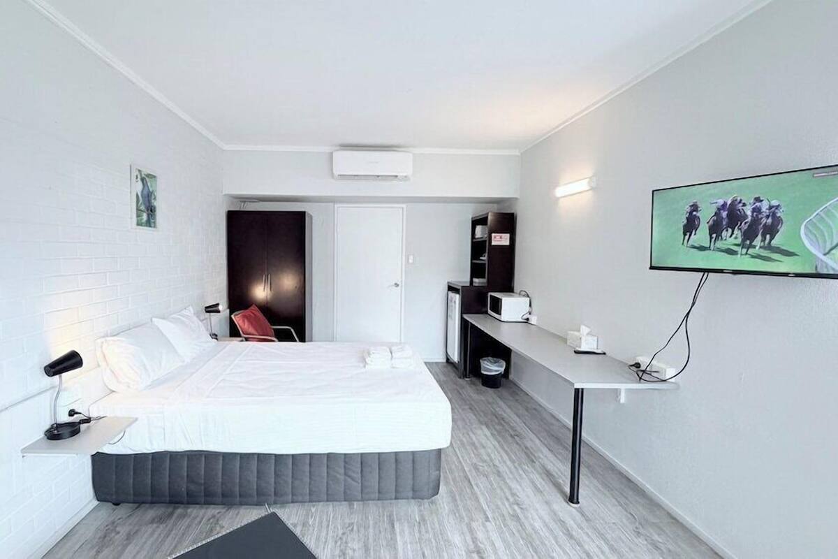 A modern hotel room with a bed, a desk, a TV, and a door leading to a bathroom.
