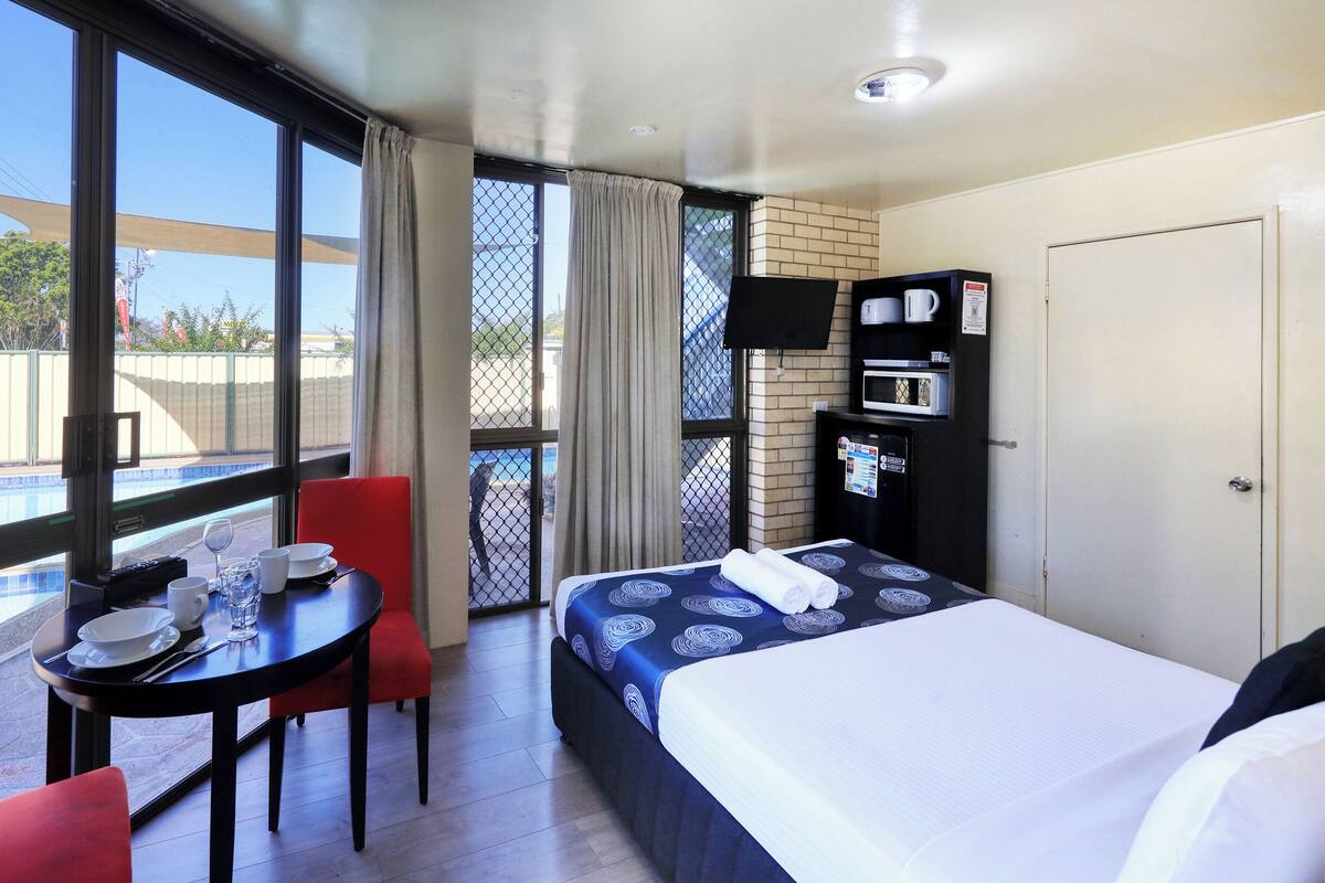 A hotel room with a bed, a dining table with chairs, a small pool, and a view of the outside.