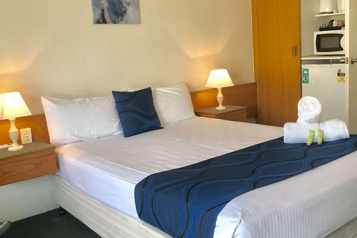 A hotel room with a bed, two bedside lamps, a painting on the wall, a wardrobe, and a microwave.