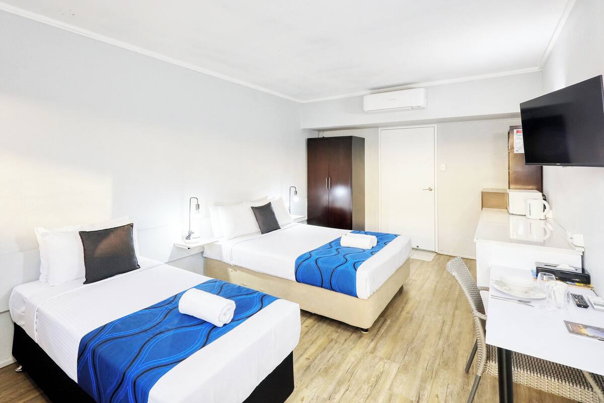 A hotel room with two beds, a desk with a chair, a television, and a door leading to another room.