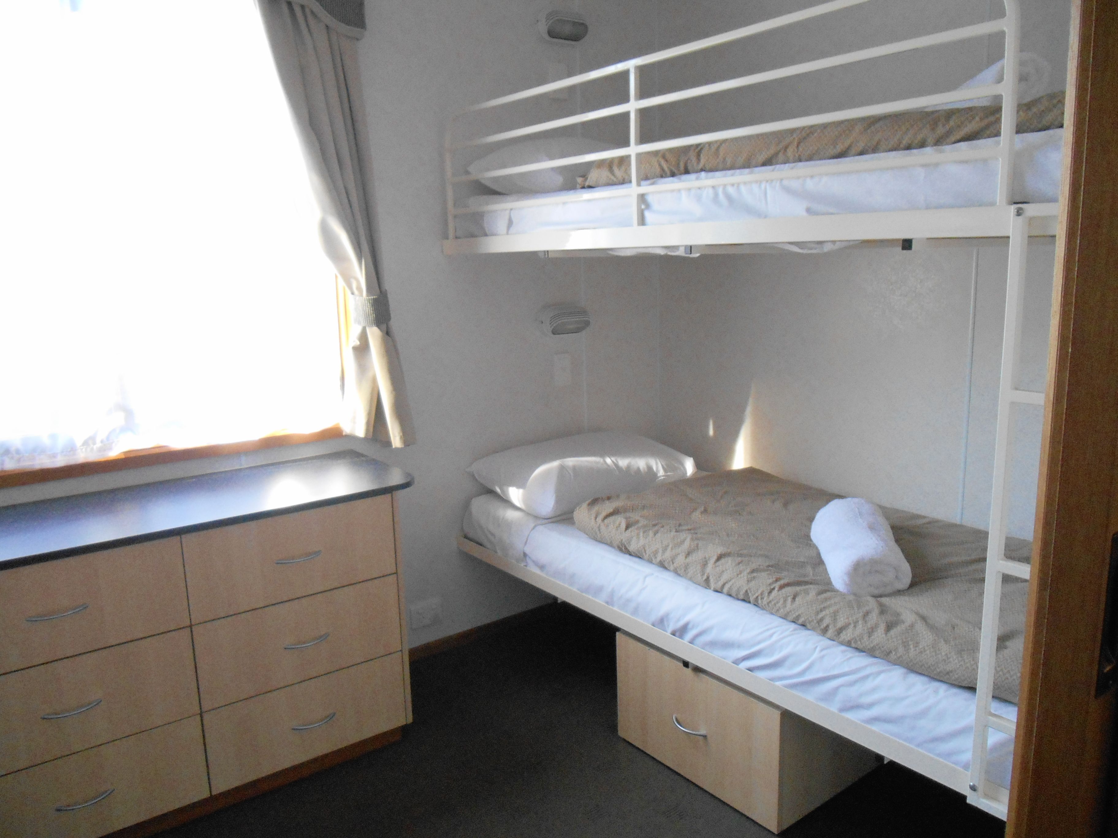 A bunk bed with a desk and drawers, a window with curtains, and a wall-mounted light fixture.