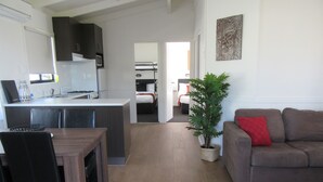 A modern living room with a sofa, a dining table, and a kitchen area with cabinets and a microwave. - Tasman Holiday Parks – Merimbula (Merimbula)