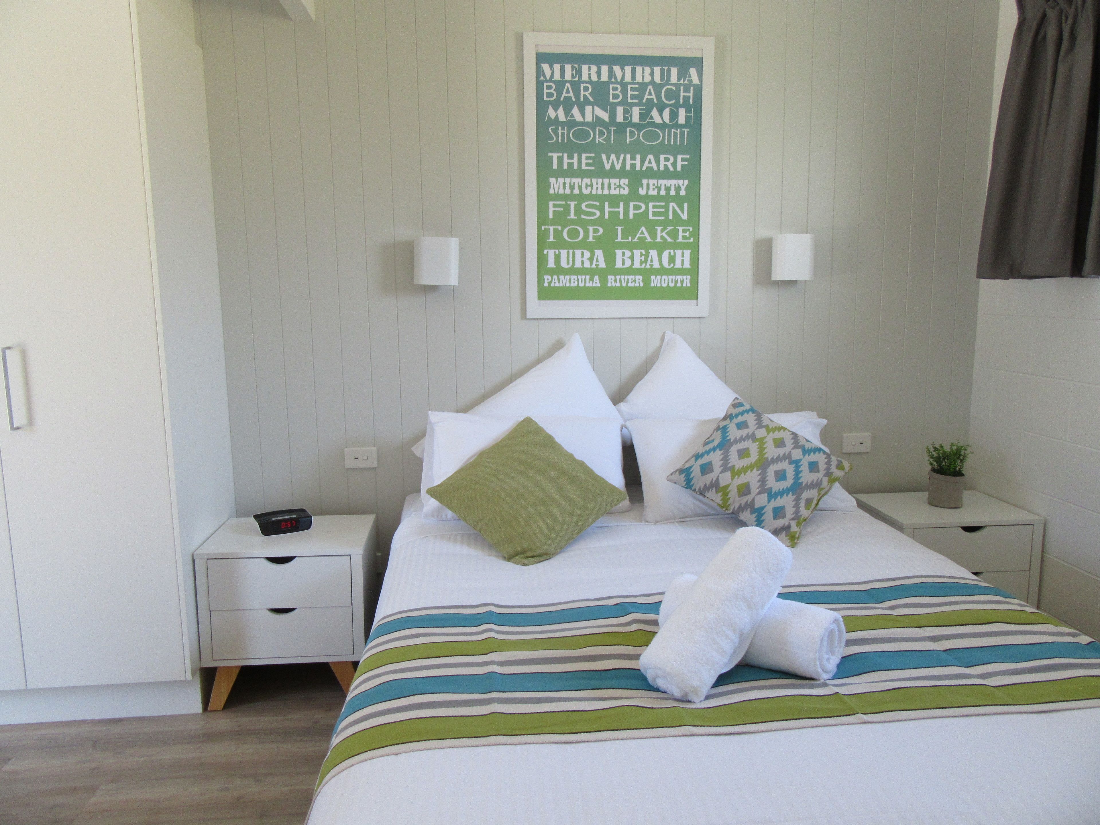 A hotel room with a neatly made bed, a bedside table with a lamp, and a wall with a sign listing local attractions.