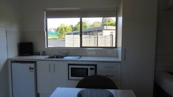 A compact kitchen with a window, a sink, a microwave, and a refrigerator.