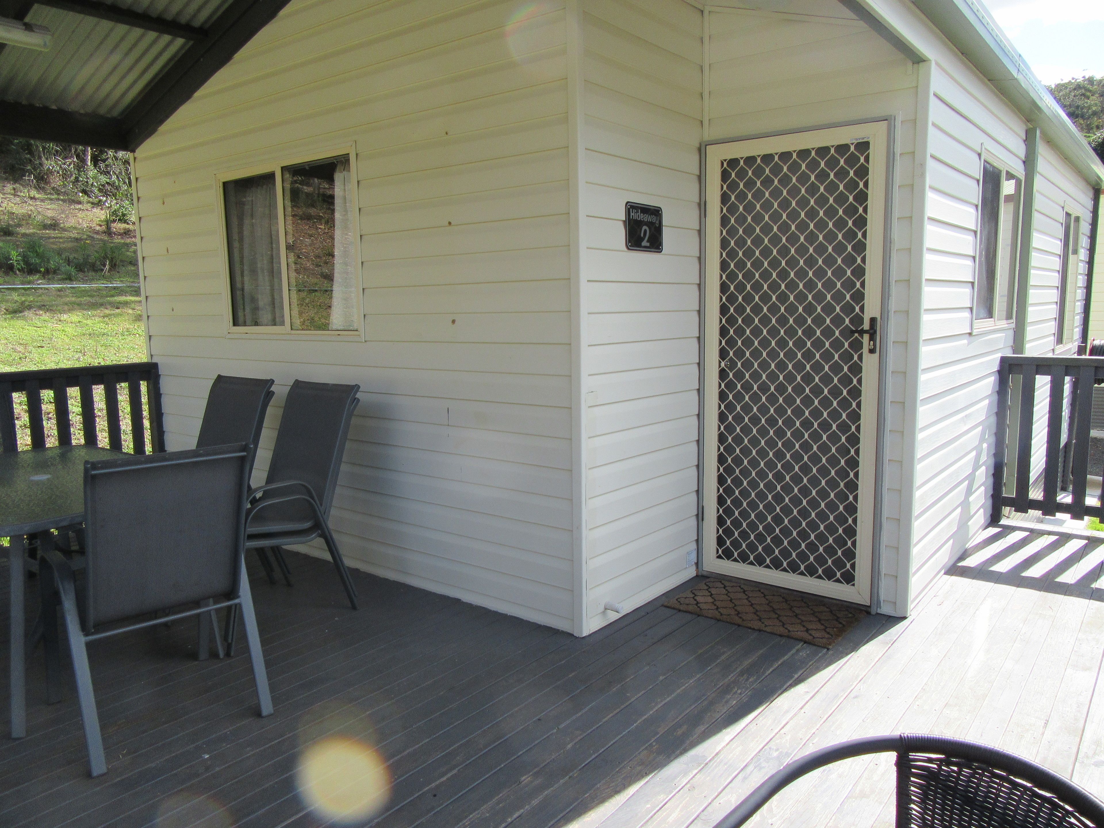 A small white cabin with a porch, a door with a mesh screen, and a table with chairs.
