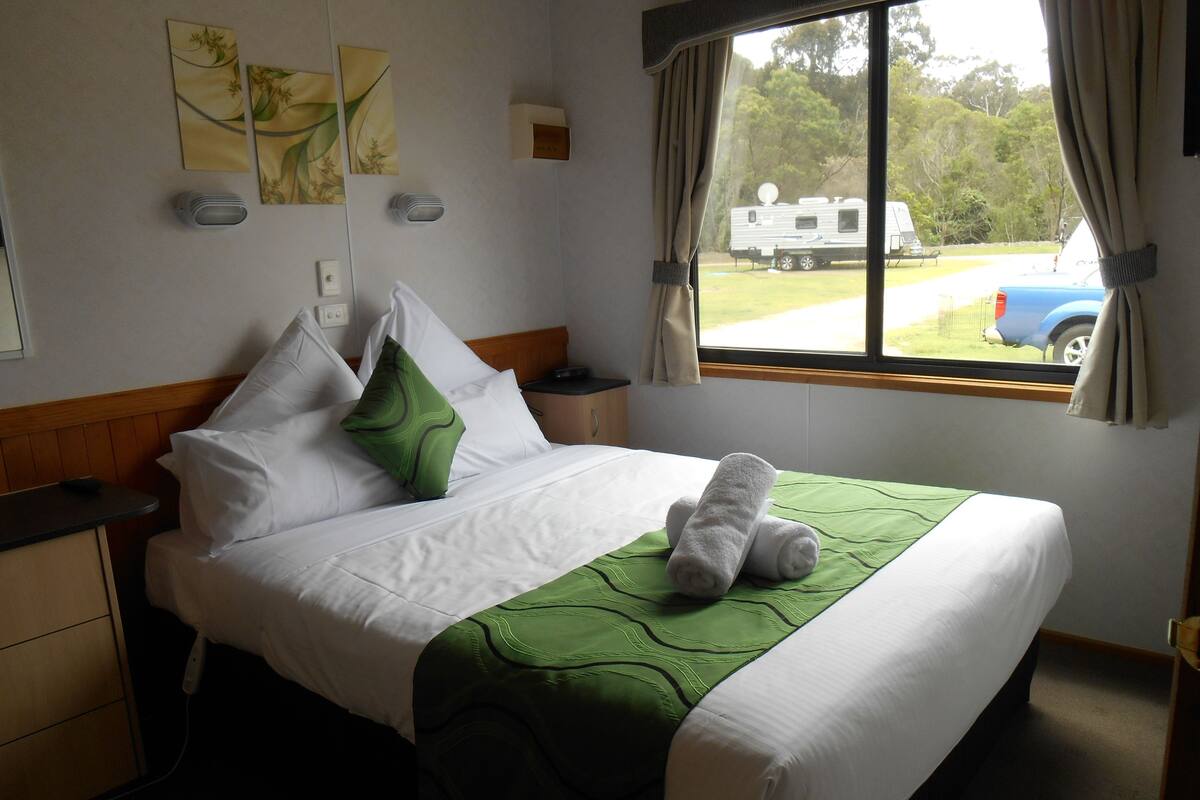 A neatly made bed with white and green bedding, a green pillow, and two rolled towels.