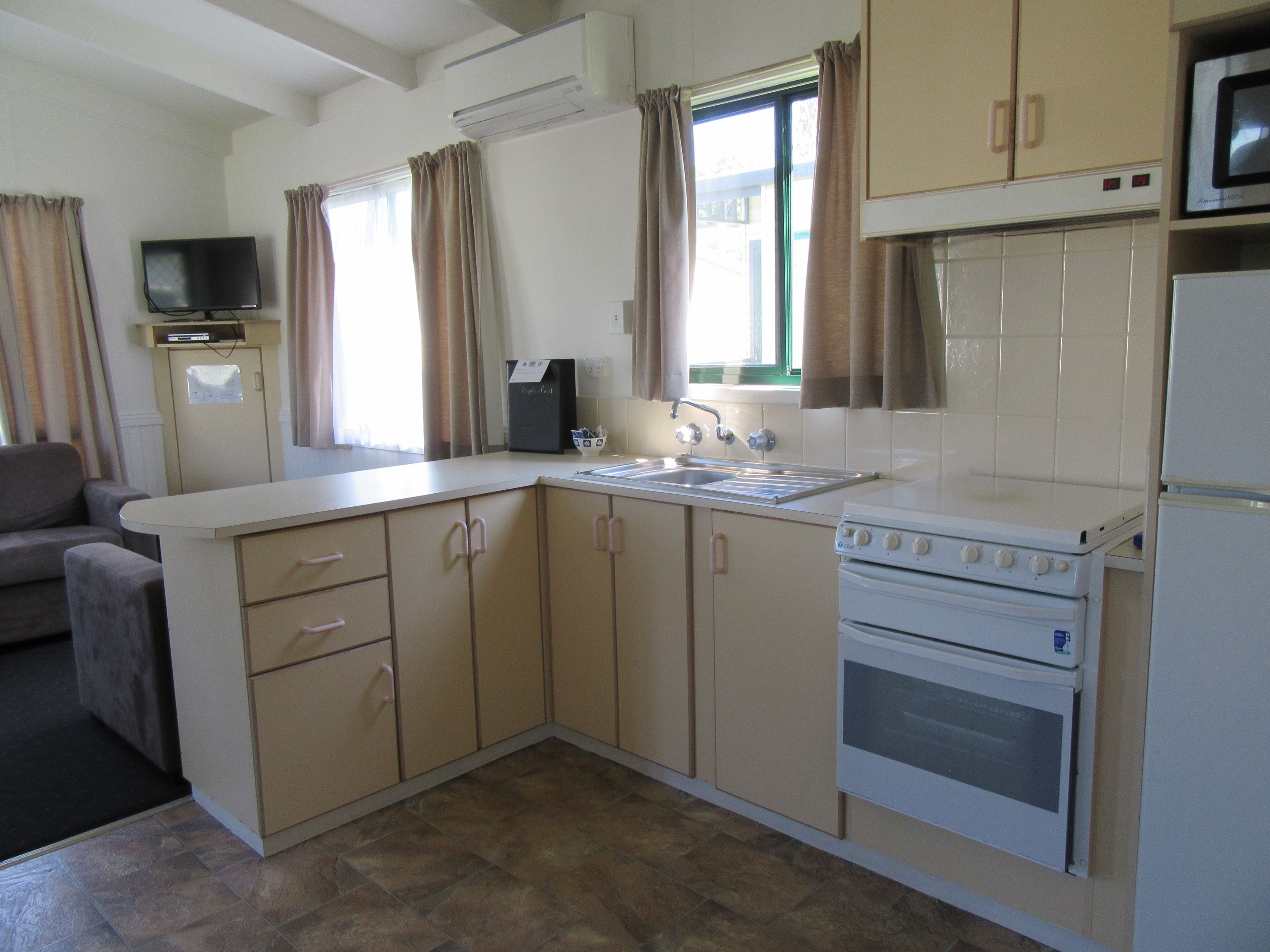 A compact kitchen with a stove, oven, sink, and a television on a cabinet.