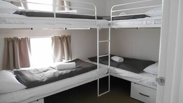 A bunk bed room with two beds, a window with curtains, and a door.