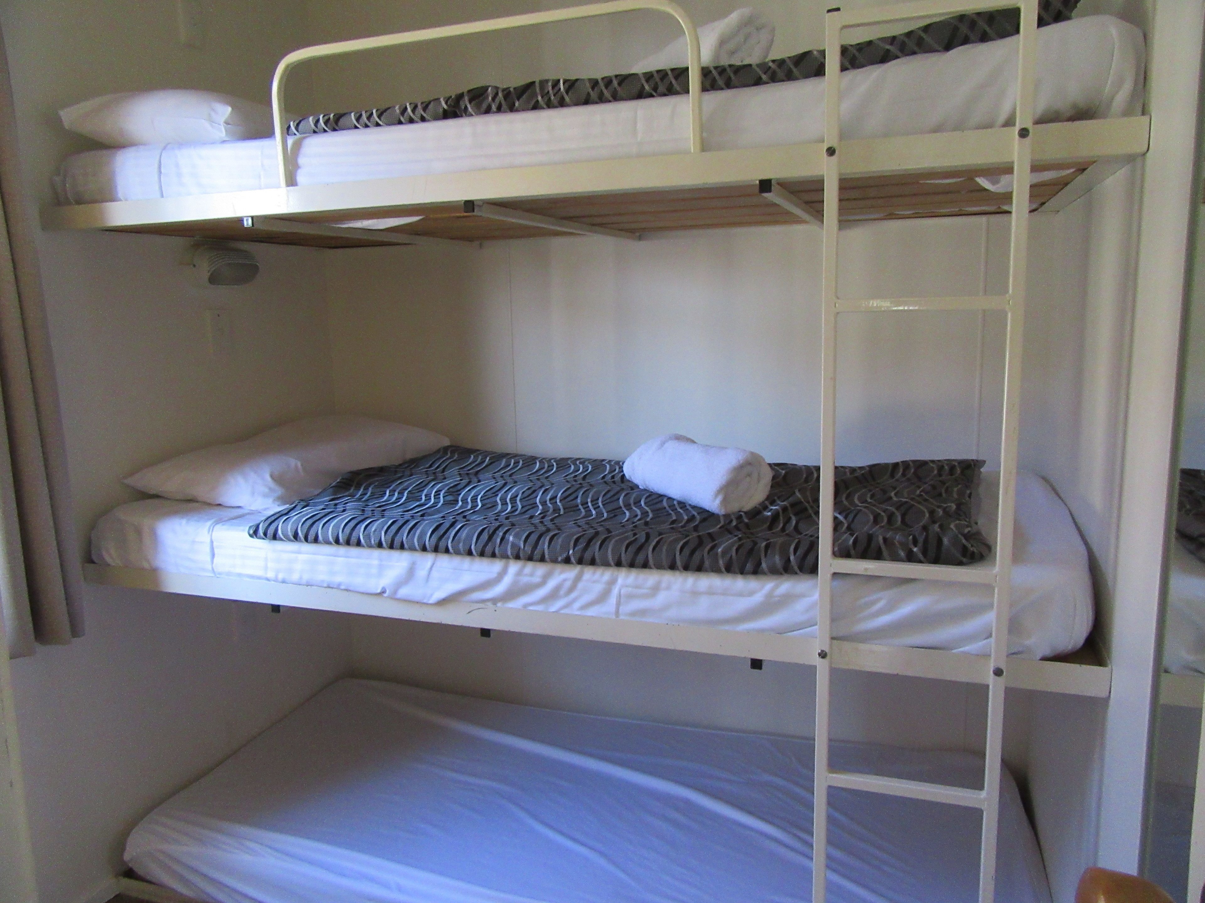 Une chambre avec un lit superposé, dotée de draps blancs et d’une couverture à motifs sur le lit du bas.