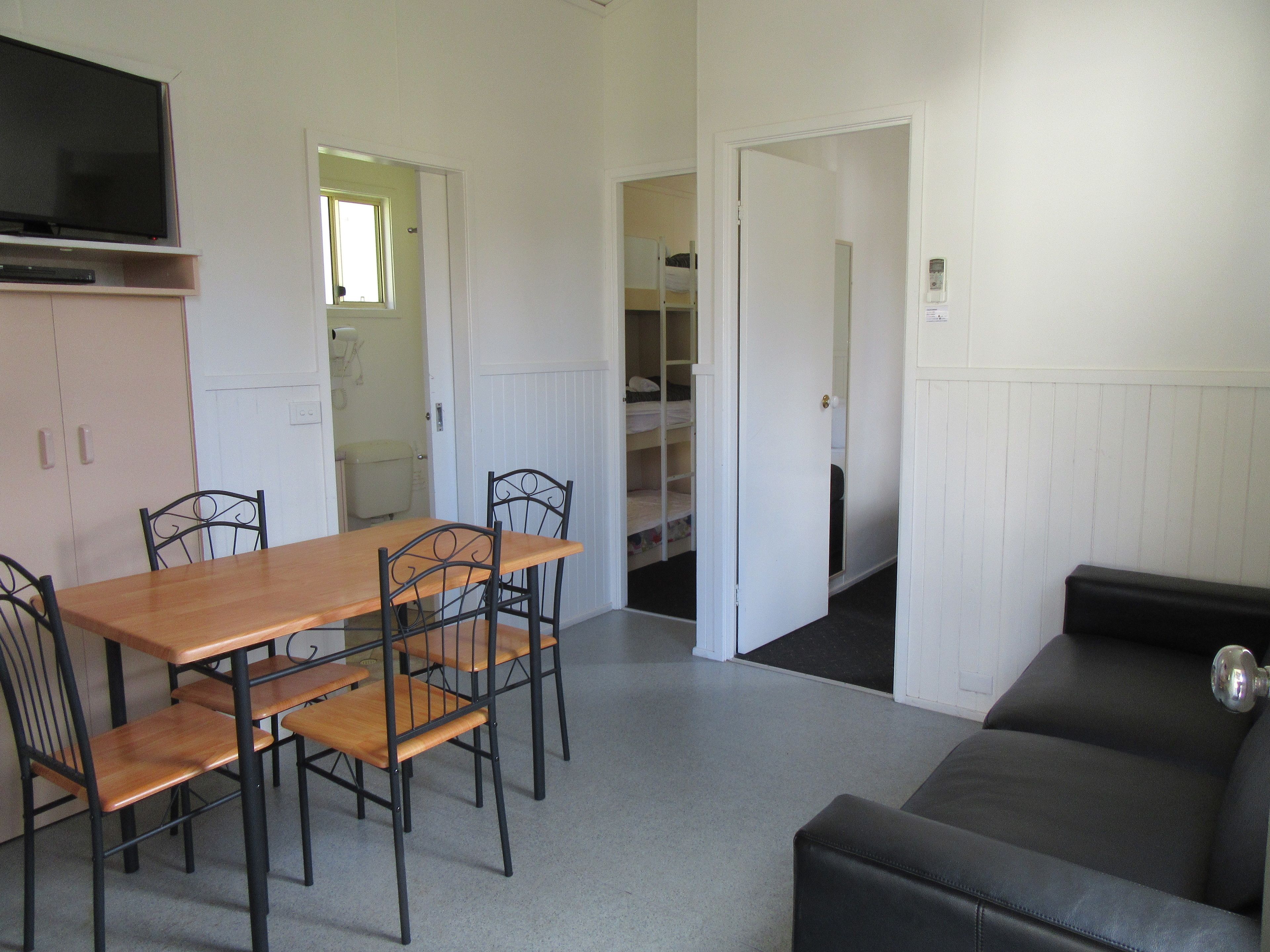 A room with a wooden dining table, four chairs, a black sofa, and a television on a stand.