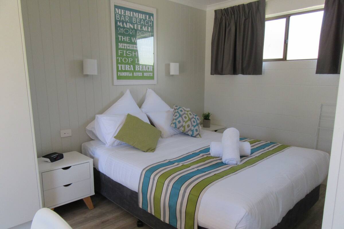 A neatly made bed with a striped blanket, a bedside table with a lamp, and a wall sign listing local attractions.