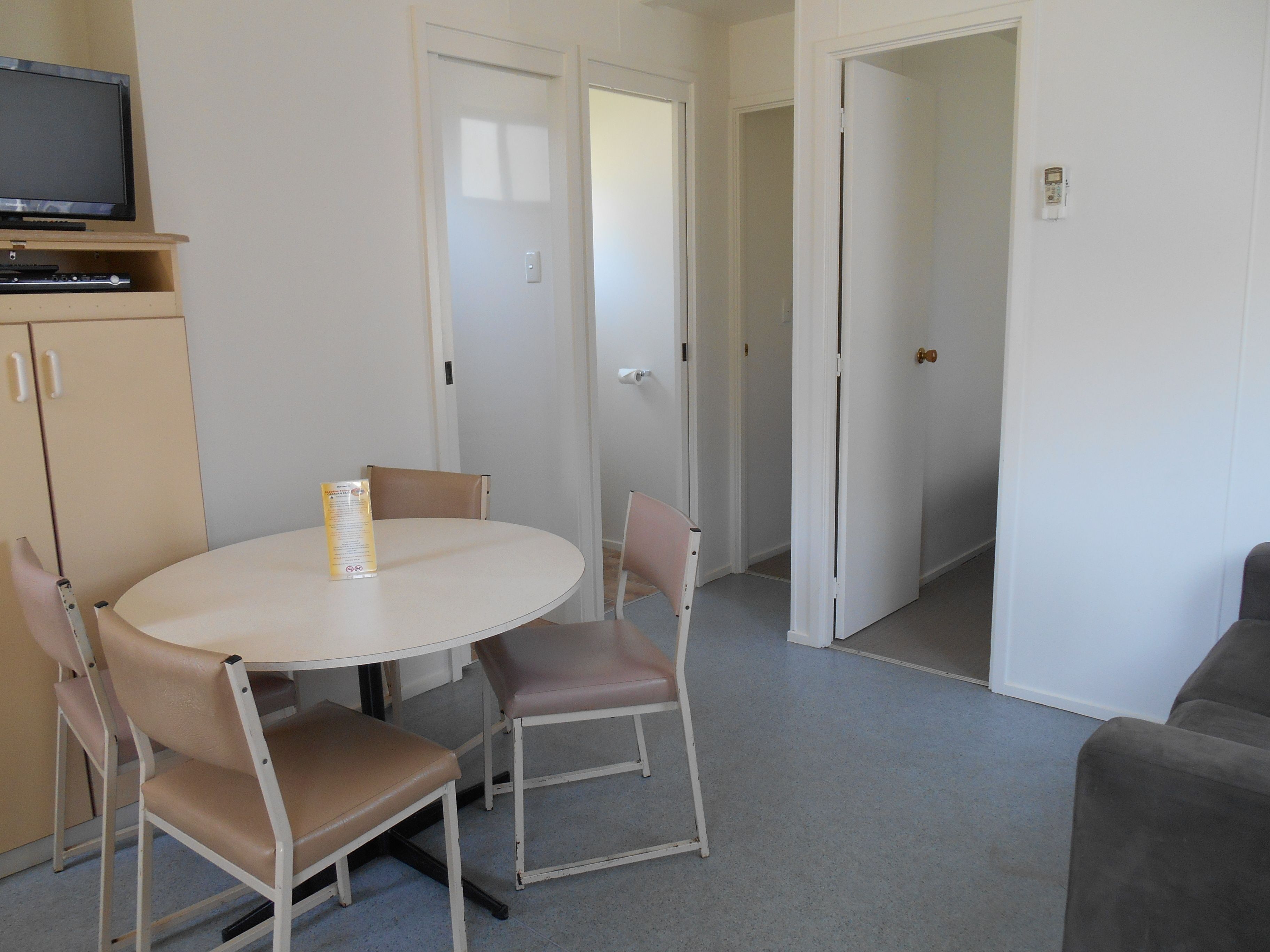 Un espacio habitable compacto con una mesa de comedor, dos sillas, un televisor sobre un mueble y una puerta que da a otra habitación.