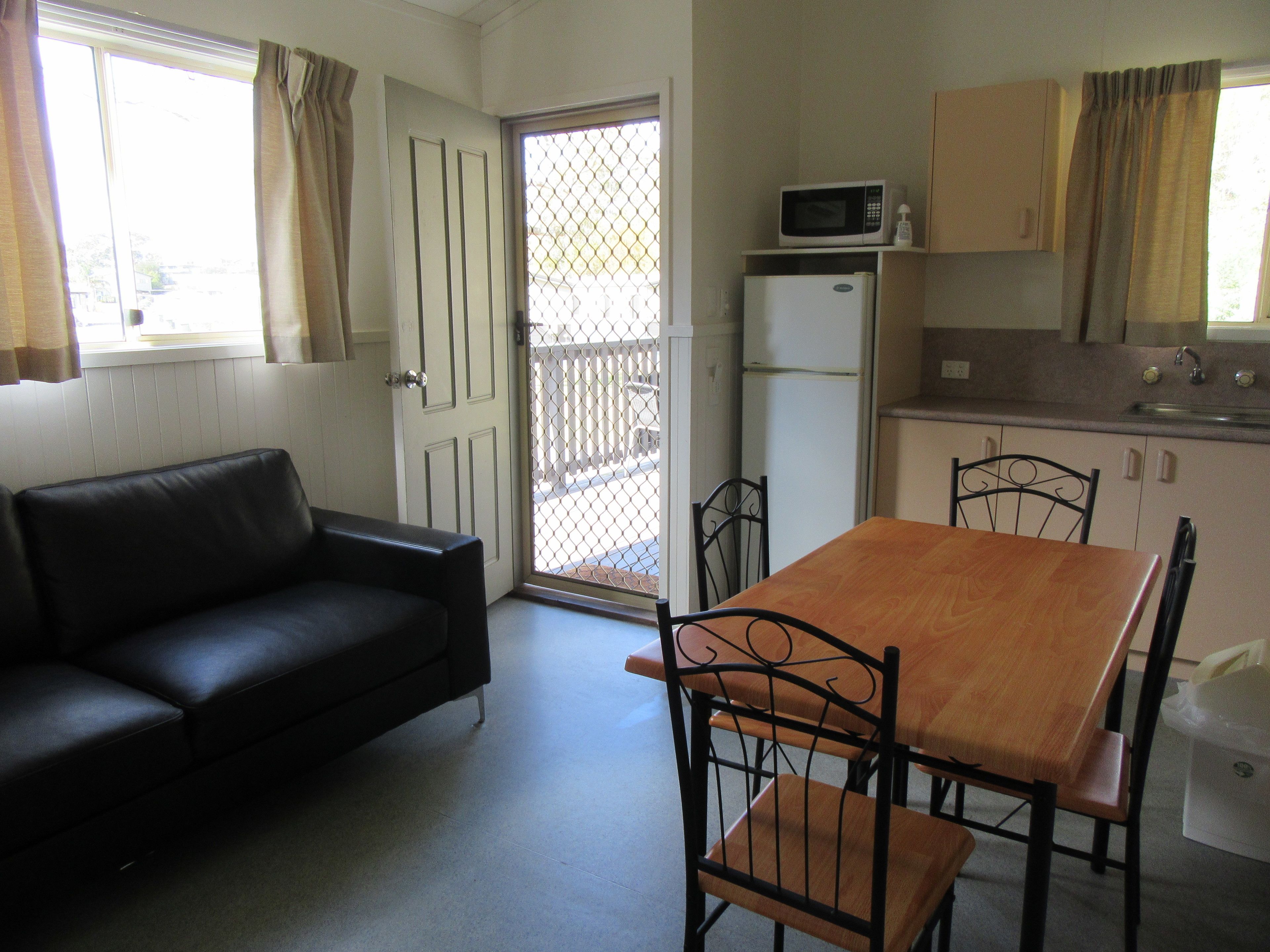 Un espacio habitable compacto con sofá, mesa de comedor, sillas, refrigerador, microondas y zona de cocina con alacenas y pileta.