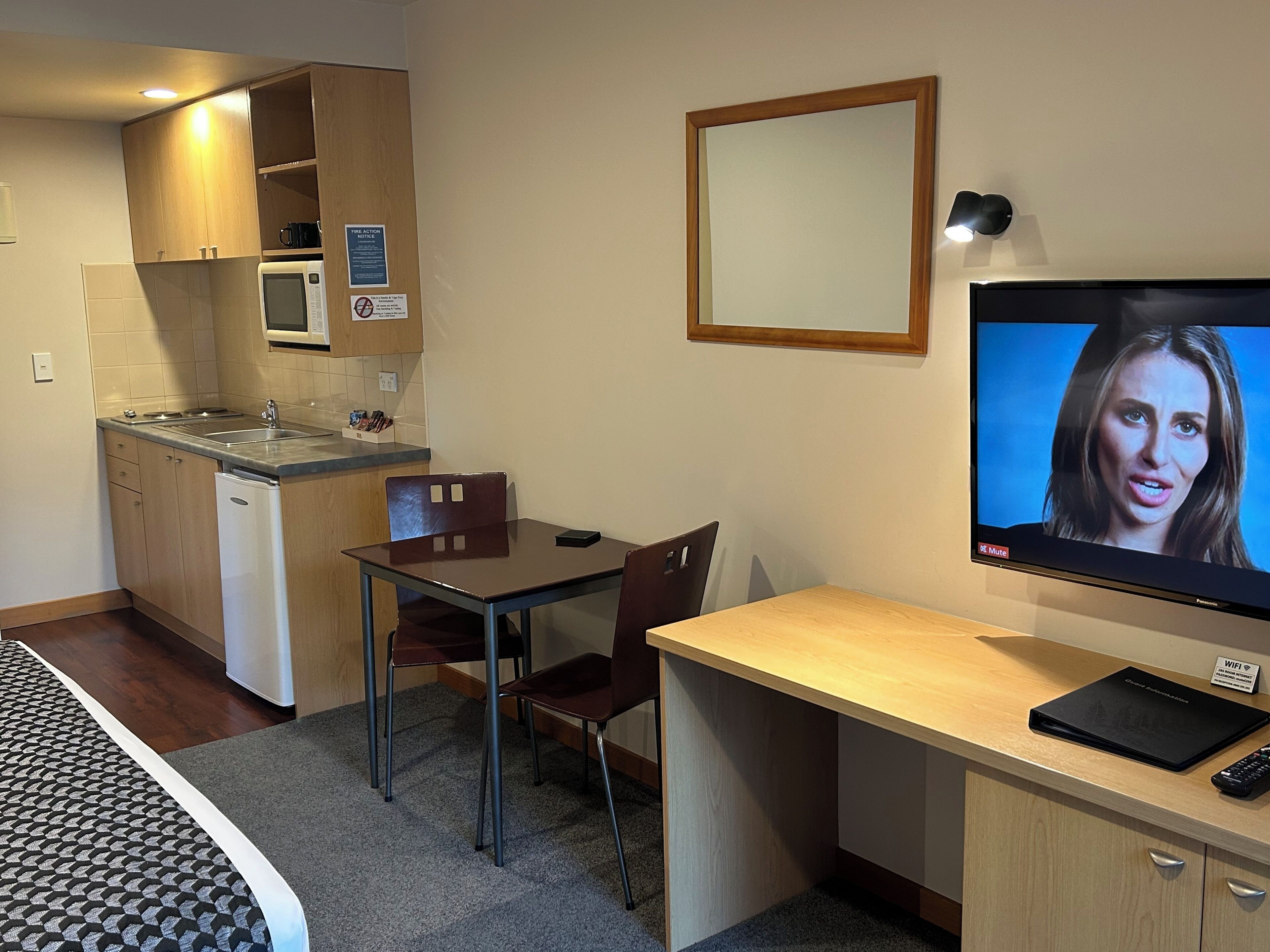 A compact hotel room with a kitchenette, a dining area, a TV, and a bed.