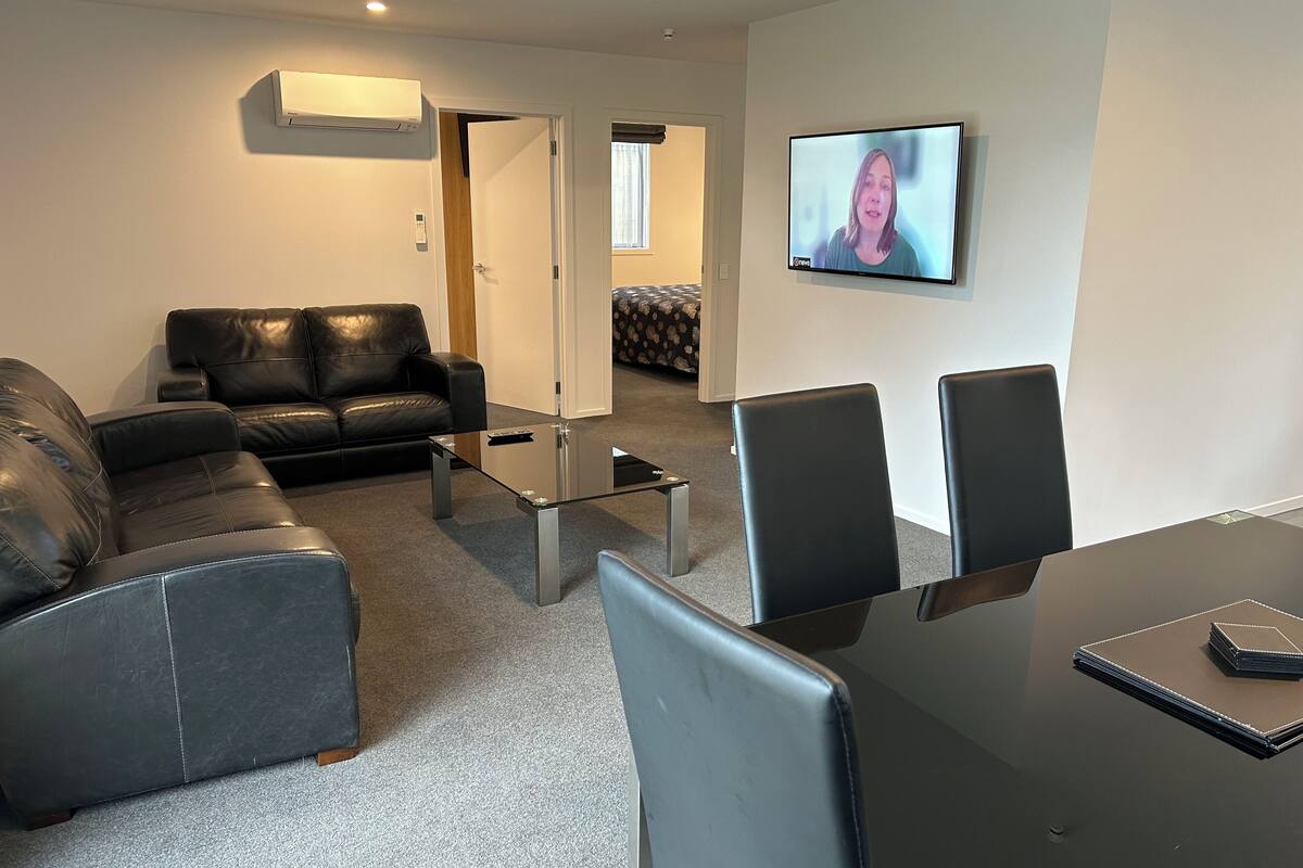 A modern living room with a glass coffee table, leather sofa, and a TV mounted on the wall.
