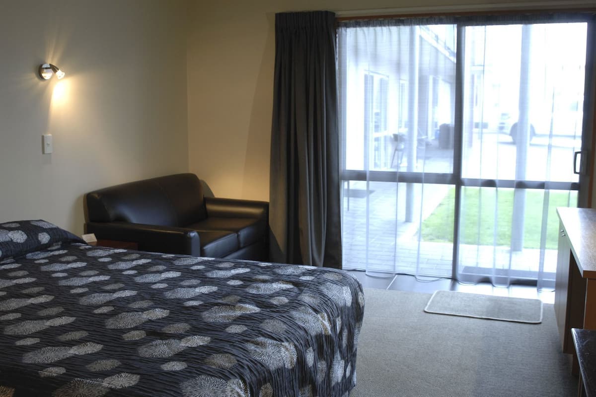A hotel room with a bed, a chair, a desk, and a view through a large window.