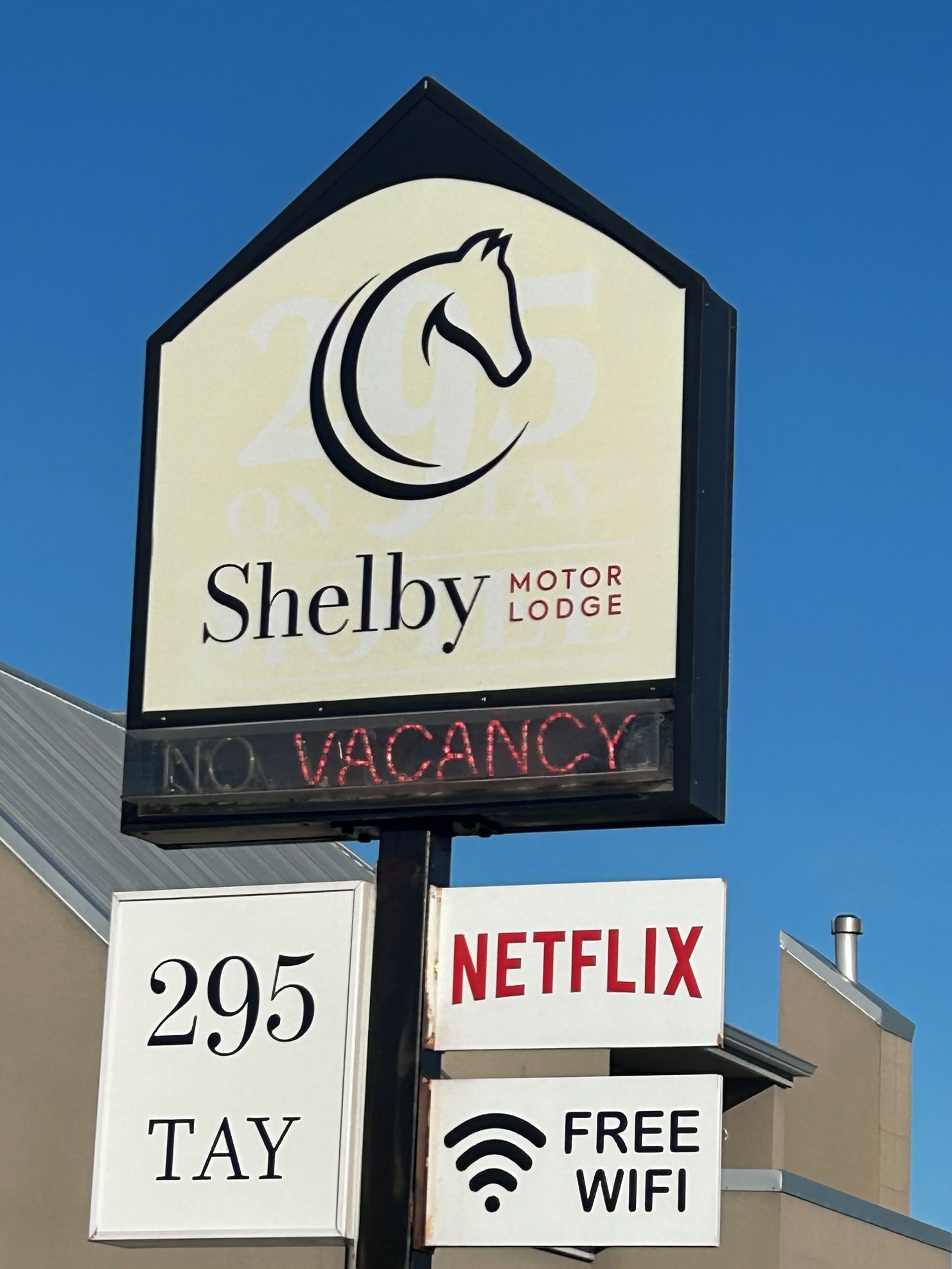 Schild für das Shelby Motor Lodge mit einem Pferdelogo, das keine freien Zimmer anzeigt. Es wirbt außerdem mit kostenlosem WLAN und Netflix.