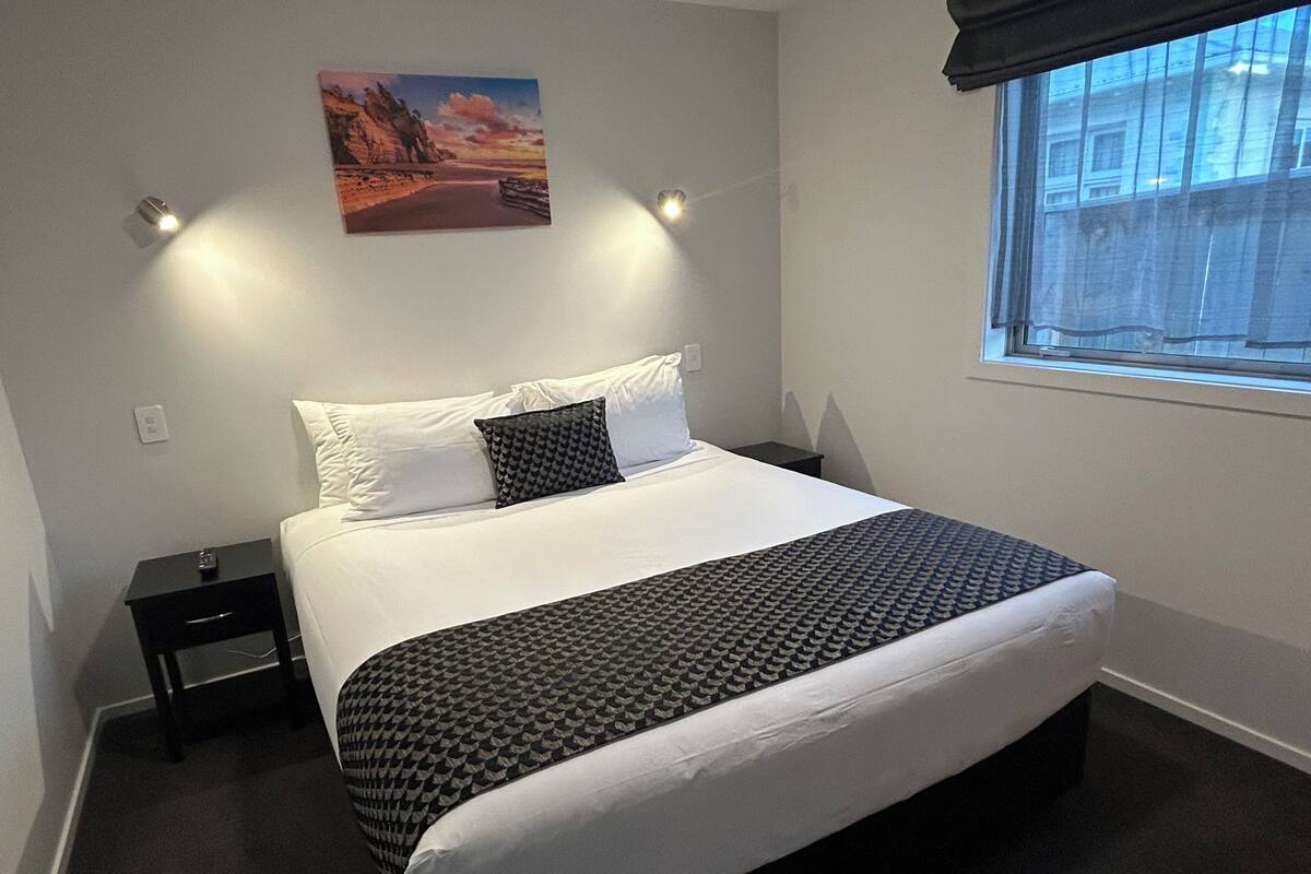 A neatly made bed with a patterned bedspread, a pillow, and a bedside table with a lamp.