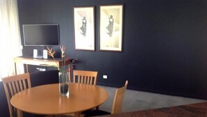 Un comedor con una mesa redonda de madera, cuatro sillas, un florero con flores, un televisor de pantalla plana sobre un mueble bajo y dos cuadros colgados en la pared.