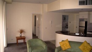 Una sala de estar con un sillón verde, un sofá verde con cojines amarillos y una pequeña mesa de madera con un jarrón.